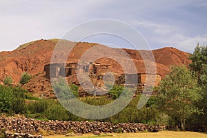 Old berber village oasis with houses build of clay bricks in front of impressive high rugged red mountain face