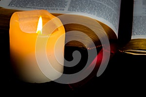 Old Bible with golden edge pages lighted by candlelight of a nearby candle