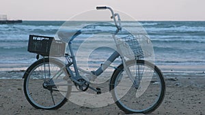 Old bicycle on the beach at sunset with storm sea and foam waves background.