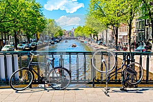 Old bicycle on the bridge in Amsterdam, Netherlands against a canal during summer sunny day. Amsterdam postcard iconic view.