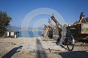 Old bicycle is leaning against aged large rusty metal structure for transporting boats in harbour under clear blue sky on mediterr
