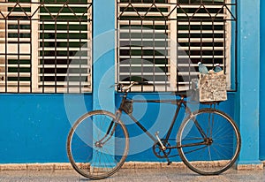 Old bicycle leaning against barred,shuttered windows and blue wall