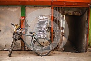 Old bicycle with stack of newspapers near rustic wall