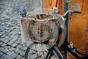 Old bicycle with wooden basket and flowers on the city street near orange wall