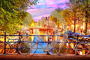 Old bicycles on the bridge in Amsterdam, Netherlands against a canal during summer twilight sunset. Amsterdam postcard iconic view