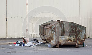 An old big rusty dumpster stands near a metal fence