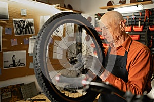 Old bike mechanic holding wheel in bicycle repair shop.