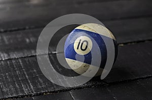 Old billiard ball number 10 striped white and blue on black wooden table background, copy space