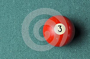 Old billiard ball number 3 red color on green billiard table, copy space