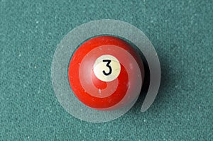 Old billiard ball number 3 red color on green billiard table, copy space