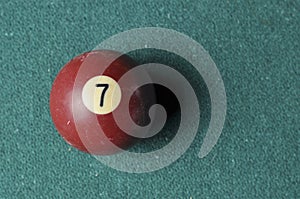 Old billiard ball number 7 brown color on green billiard table, copy space