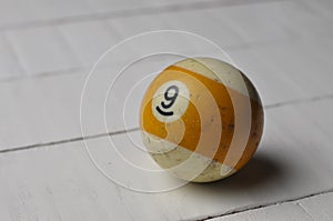 Old billiard ball number 9 striped white and yellow on white wooden table background, copy space