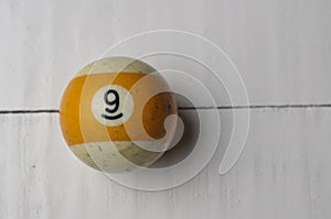 Old billiard ball number 9 striped white and yellow on white wooden table background, copy space