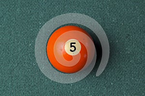 Old billiard ball number 5 orange color on green billiard table, copy space