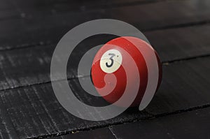 Old billiard ball number 3 red color on black wooden table background, copy space