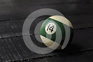 Old billiard ball number 14 striped white and green on black wooden table background, copy space