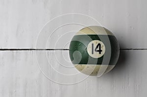 Old billiard ball number 14 striped white and green on white wooden table background, copy space