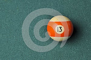 Old billiard ball number 13 striped white and orange on green billiard table, copy space
