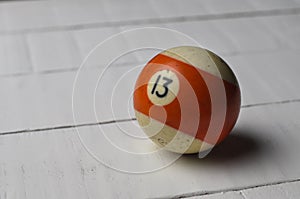 Old billiard ball number 13 striped white and orange on white wooden table background, copy space