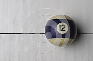 Old billiard ball number 12 striped white and purple on white wooden table background, copy space