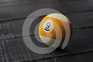 Old billiard ball number 9 striped white and yellow on black wooden table background, copy space
