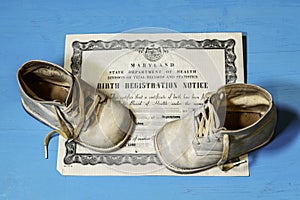 Old birth certificate and white baby shoes on blue