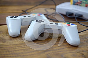 Old 8-bit video game console with game cartridge and two gaming joysticks on wooden background