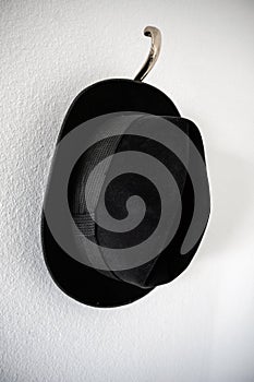 Old black hat hanging on hook at wall