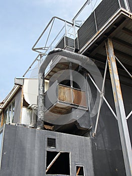 Old black industrial building with rusting steel girders tanks and pipes and railings against a blue sky