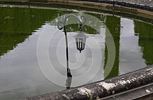 Old black iron street lantern in the park against the background of reflections in the water