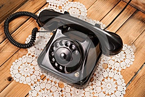 Old black phone on lace tablecloths and wooden background