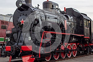 Old black and red retro steam locomotive at the railway station. Vintage train staying on the railroad.