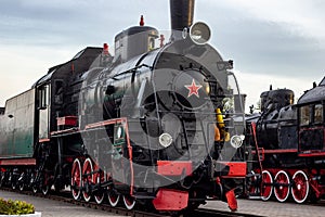 Old black and red retro steam locomotive at the railway station. Vintage train staying on the railroad.