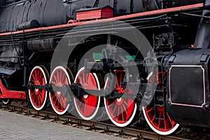 Old black and red retro steam locomotive wheels at the railway station. Vintage train staying on the railroad.