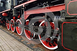 Old black and red retro steam locomotive wheels at the railway station. Vintage train staying on the railroad.