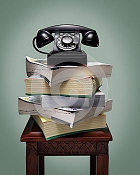 Old black rotary dial telephone on stack of phone books