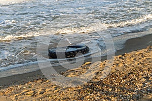 Old black rubber tire left on beach, environment pollution concept, selective focus, color toned picture. Discarded old tyre in bl