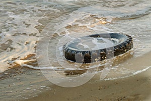 Old black rubber tire left on beach, environment pollution concept, selective focus, color toned picture. Discarded old tyre in bl