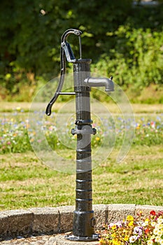 Old black street water pump. Usually the water from such pumps is not potable. In the background street and buildings painted in d