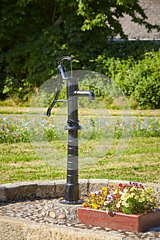 Old black street water pump. Usually the water from such pumps is not potable. In the background street and buildings painted in d