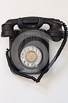 Old black telephone hanging on a white wall