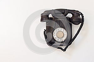 Old black telephone hanging on a white wall