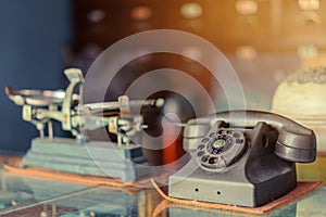 The old black telephone with rotary dial with dust and scratches placed on a clear glass cabinet