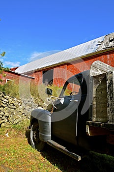 Old black truck in front of old red barn