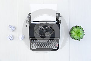 Old black typewriter with blank sheet of paper on wooden desk