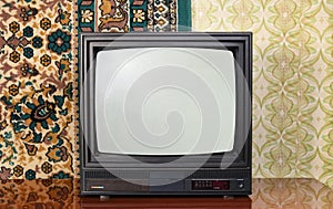 Old black vintage TV set against wallpaper and carpet 1980-1990 background.