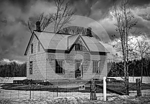 Old black and white abandoned spooky looking farmhouse in winter on a farm yard in rural Canada