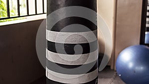 An old black and white punching bag with a blue exercise ball nearby, inside a hardcore gym