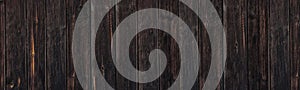 Old blacked knotty wooden board wide banner texture. Aged rough dark wood plank fence. Dark rustic large background