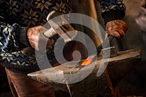 Old blacksmith manually forging molten metal with hammer on the anvil